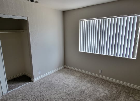 Carpeted bedroom with large window and closet at Lakeshore Terrace Apartments in Lakeside, California.