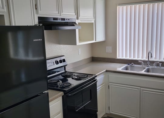 Kitchen with spacious white cabinets, black appliances and large window at Lakeshore Terrace Apartments in Lakeside, California.