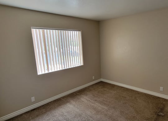 Carpeted bedroom with large window at Lakeshore Terrace Apartments in Lakeside, California.
