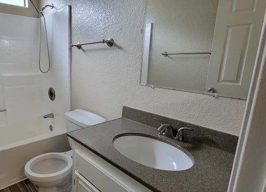 Bathroom with plank style flooring, window, white fixtures and large mirror at Lakeshore Terrace Apartments in Lakeside, California.