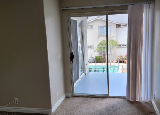 Carpeted bedroom with sliding glass door to porch and view of swimming pool at Lakeshore Terrace Apartments in Lakeside, California.