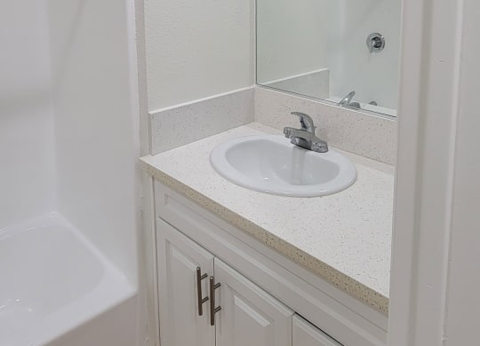 Bathroom sink with white cabinets and large mirror in one bedroom apartment at the Atrium Apartments in San Diego, CA.