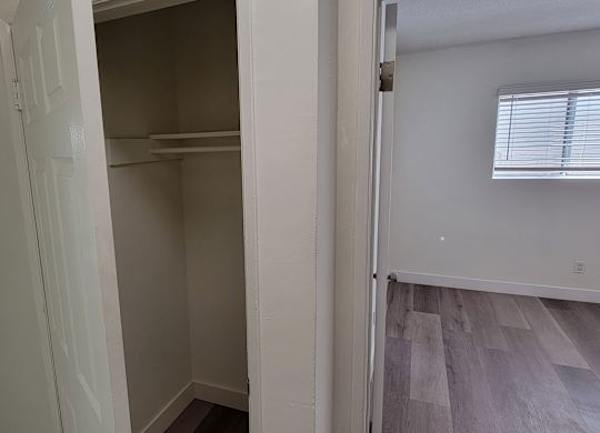 A white closet with a shelf and a window with blinds.