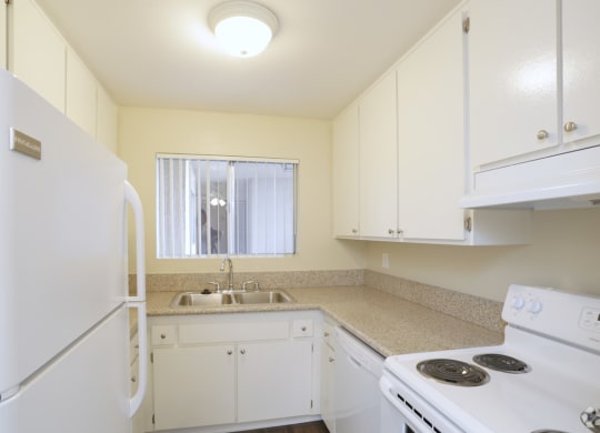 Kitchen with white appliances including refrigerator, dishwasher, and electric range at Villa Pacific Apartments in Oceanside, California.