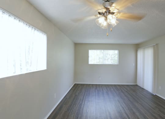 Dining araa with ceiling fan and living room with plank style flooring and lots of windows for natural light at Villa Pacific Apartments in Oceanside, California.