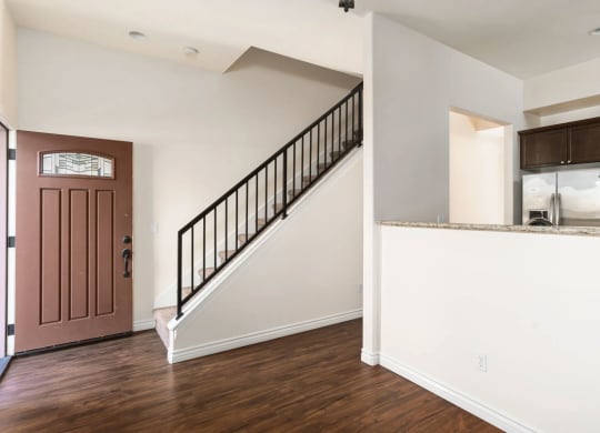 Front entrance with wood style laminate flooring and view of open kitchen with dark wood cabinetry at The Nines Townhomes in Escondido, California.