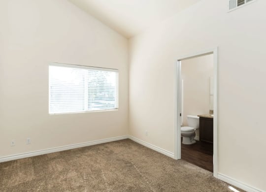 Carpeted bedroom with cathedral ceiling, larage window and bathroom at The Nines Townhomes in Escondido, California.