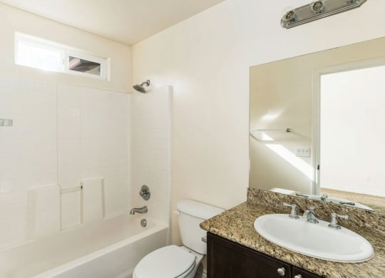 Bathroom with granite slab vanity counter top, white fixtures, upgraded faucets, and privace window for natural light at The Nines Townhomes in Escondido, California.
