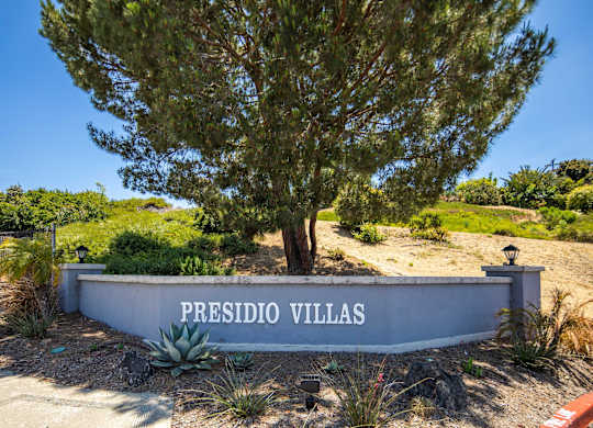 A sign that says "Presidio Villas" in front of a tree.