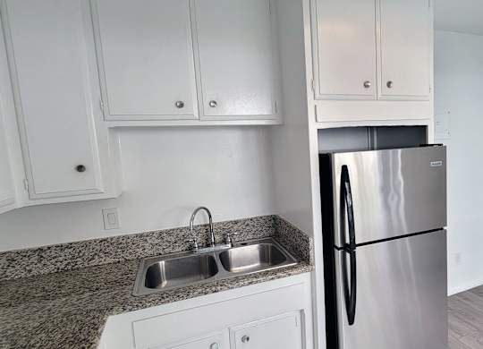 A kitchen with a granite countertop and a stainless steel refrigerator.