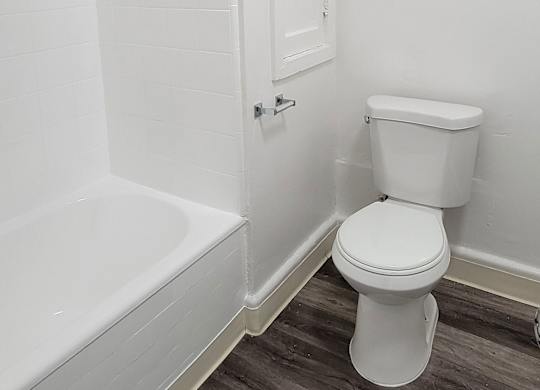 A white toilet in a bathroom with a white tub and shower at the Western At Rosewood apartments..