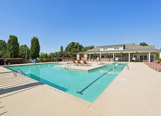 A large swimming pool with lounge chairs and a building in the background.