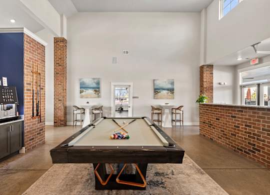 A pool table is in the middle of a room with a brick wall.