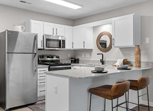 A kitchen with a refrigerator, microwave, oven, and bar stools.