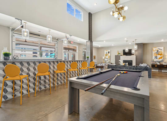 a clubhouse with a pool table and a bar with yellow chairs