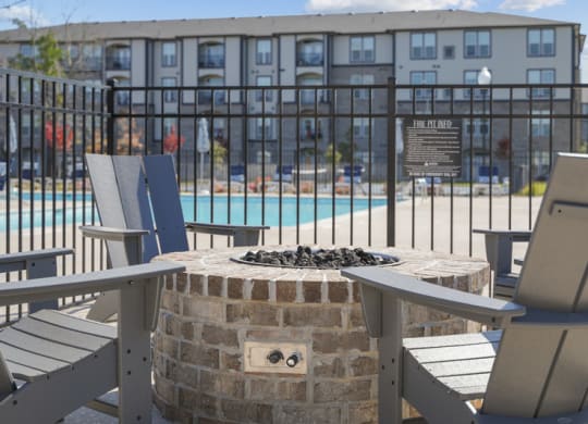 a fire pit with two chairs and a table in front of a swimming pool