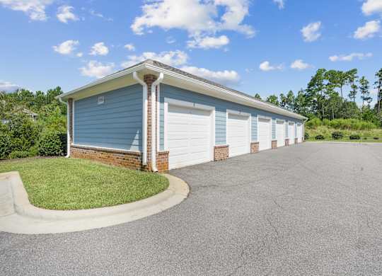A blue building with a white garage door is surrounded by a paved driveway.