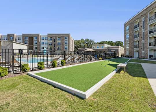 A grassy area in front of apartment buildings with a pool and a small pavilion.