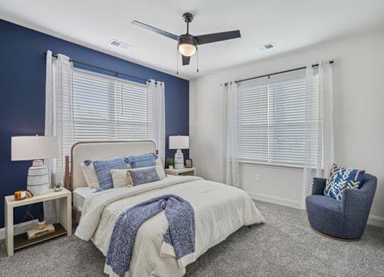 A bedroom with a bed, chair, and ceiling fan.