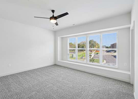 A room with a ceiling fan and a window showing a view of a residential area.