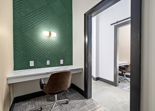 a room with a desk and a chair in front of a wall with green wallpaper