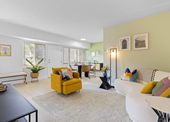 a living room with a white couch and yellow chair and a dining room table in the background