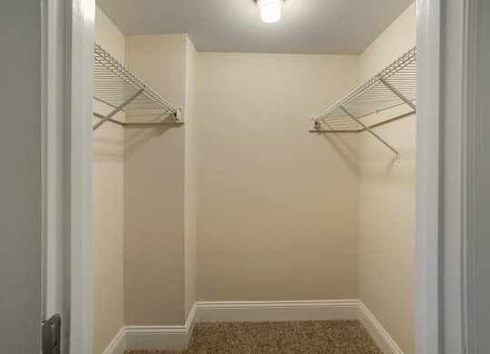 a walk in closet in a home with white walls and shelves and a white door