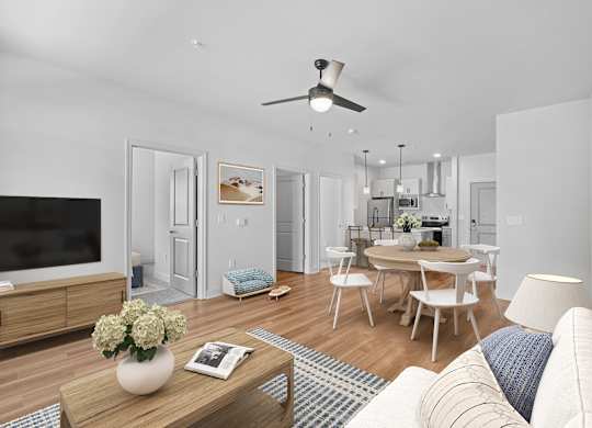 A modern living room with a flat screen TV, a dining table with chairs, and a kitchen area in the background.