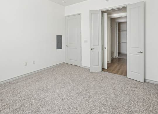 A room with white walls and carpeted floor with two doors.