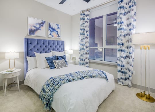 a bedroom with a bed and a window with blue and white curtains