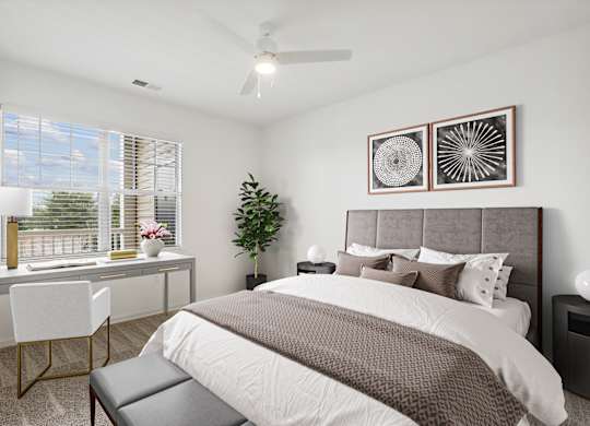 A bedroom with a large bed, a desk with a chair, and a potted plant.