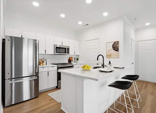 A modern kitchen with a white island and black bar stools.