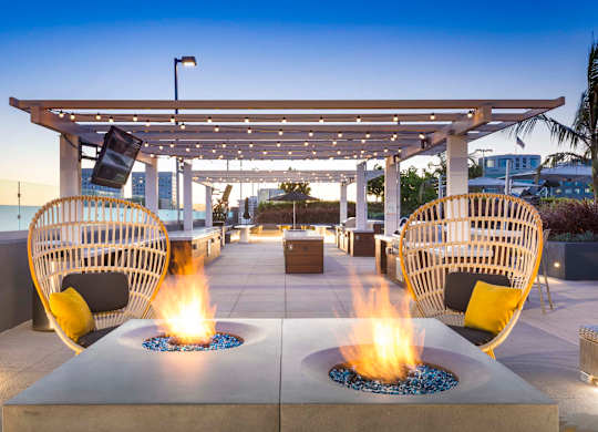 Rooftop fire pit lounge with wicker chairs and pergola at Elements Apartments, Irvine, CA
