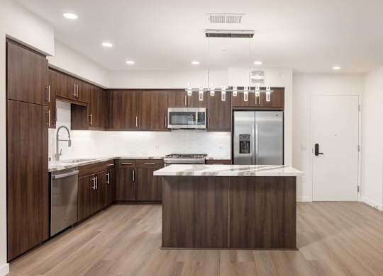 Kitchen with dark wood cabinetry and marble island at Elements Apartments, California