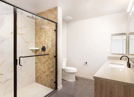 Bathroom with glass enclosed shower and textured tile accent at Elements Apartments, California, 92612