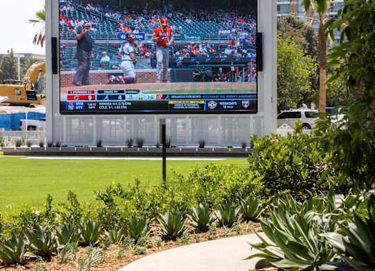 Large outdoor video screen by landscaped lawn and walkway at Elements Apartments, Irvine
