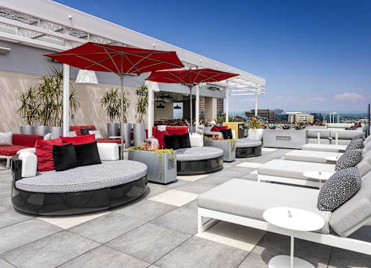 Rooftop lounge with red umbrellas and white seating at LUX by Garden* Apartments, San Diego, CA