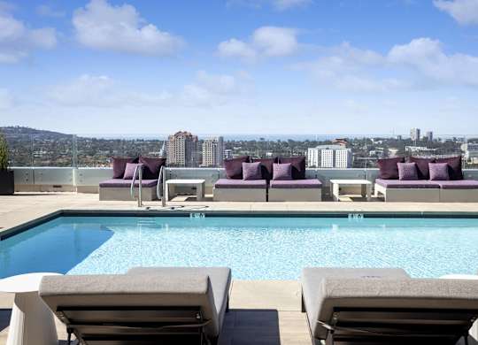 Rooftop pool with skyline views and purple cushioned seating at LUX by Garden* Apartments, San Diego, California