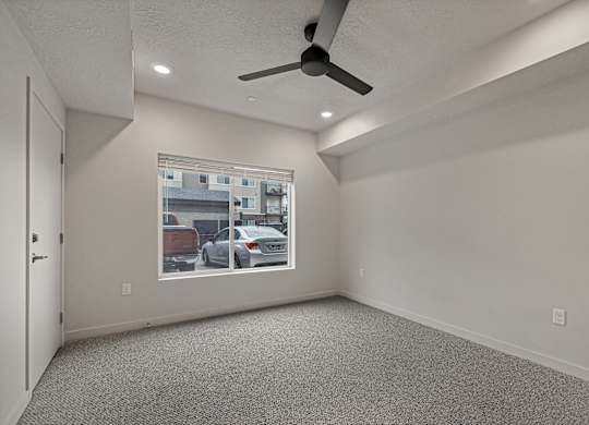 A room with a ceiling fan and a window showing a parking lot outside.
