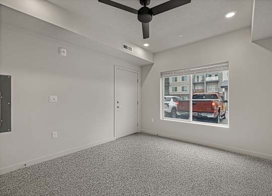 A room with a ceiling fan and a window showing a street view.