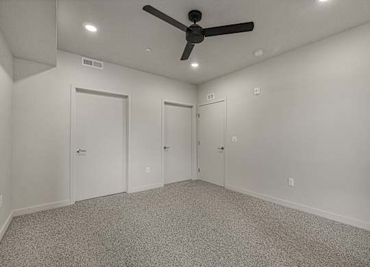 A room with a ceiling fan and three doors.