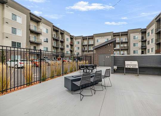 A patio with a table and chairs is surrounded by a black fence and apartment buildings.
