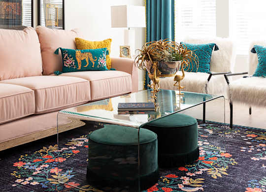 A living room with a pink couch, a glass coffee table, and a floral rug.
