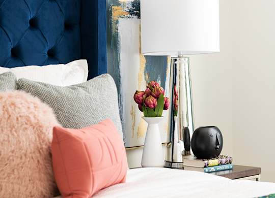 A bed with a blue headboard and a white lamp on a side table.