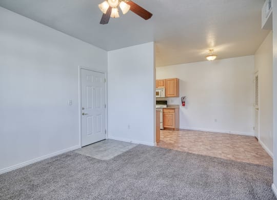 a living room with a ceiling fan and a kitchen in the background