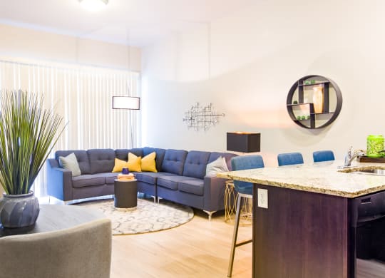 a living room with blue couches and a kitchen with a bar and a table at Sugar House Apartments By Urbana, Salt Lake City, UT, 84105