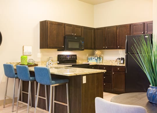 a kitchen with an island with bar stools and a black refrigerator at Sugar House Apartments By Urbana, Salt Lake City, UT, 84105