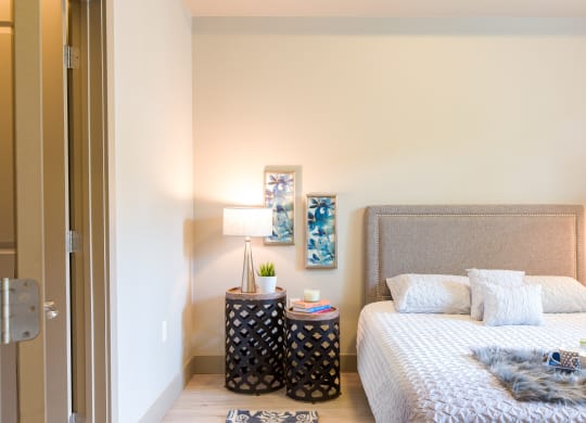 a bedroom with a bed and a nightstand with plants and a lamp at Sugar House Apartments By Urbana, Salt Lake City, UT, 84105