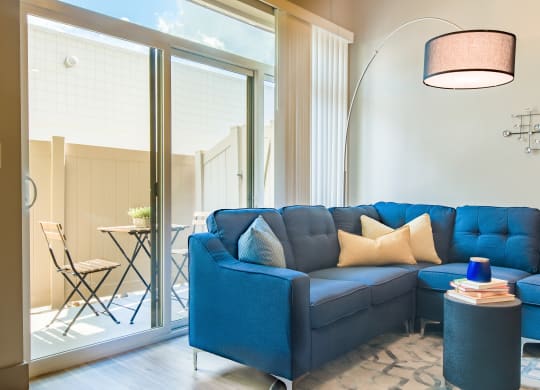 a living room with a blue couch and a large window at Sugar House Apartments By Urbana, Salt Lake City, UT, 84105