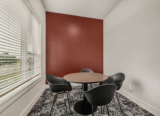 A room with a round table and chairs by a window.